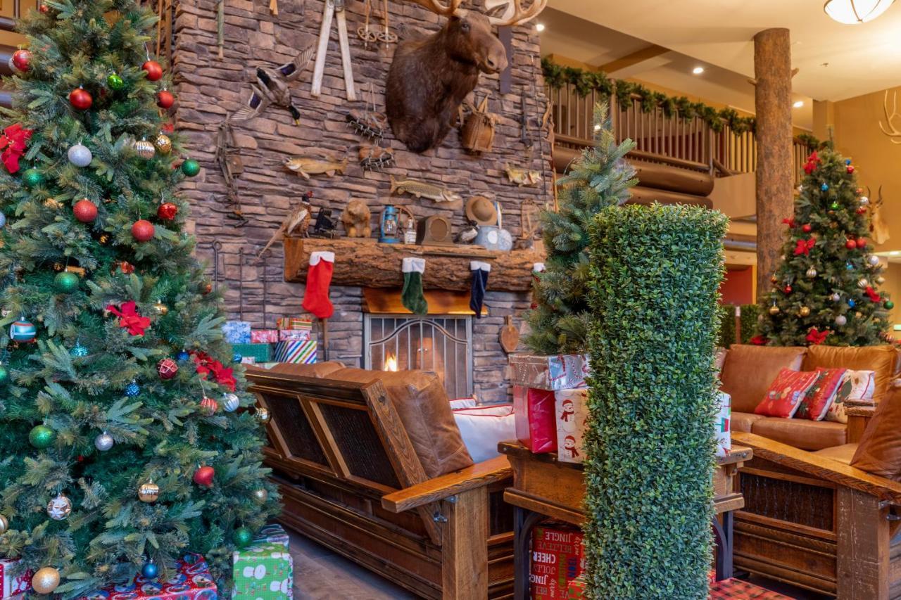 فندق ذا جراند آت جراند كانيون توسايان المظهر الخارجي الصورة The photo shows a cozy holiday scene with a rustic aesthetic. In the center, there is a wooden bench in front of a stone fireplace, which is adorned with festive decorations. Above the fireplace, a mounted moose head adds a touch of wilderness charm.