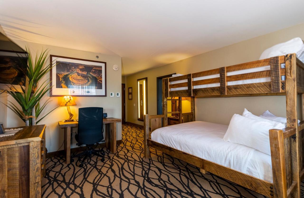 فندق ذا جراند آت جراند كانيون توسايان المظهر الخارجي الصورة The photo shows a cozy hotel room. It features a bed with white bedding and a wooden headboard. Beside the bed, there is a bunk bed structure, though it is currently not occupied. A desk with a chair is positioned against one wall, and there is a lar